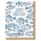 Greeting card with kraft envelope. Reads "happy birthday" in hand-written, serif font, surrounded by illustrated fish of various sizes and shapes. Shades of blue.