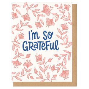 A greeting card and envelope featuring pink gradient flowers surrounding navy blue script that reads "I'm so grateful."