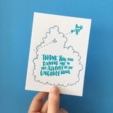 white greeting card with an illstration of an aeroplane flying through a cloud, teal hand-lettering on the cloud reads "thank you for driving me to the airport at an ungodly hour" photogrpahed hand-held in front of a blue background