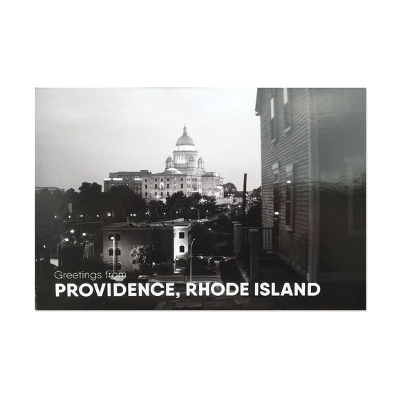 postcard of a black and white photograph of the RI state house at night behind some buildings and trees. white text reads 