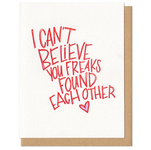 A greeting card and envelope featuring hand letter text in red that reads "I can't believe you freaks found each other" with a pink heart below.