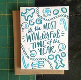 A greeting card and envelope featuring cookies, ornaments, and garland with text in the center that says "it's the most wonderful time of the year."