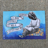 postcard of a blue, grey, and orange illustration of a fellow reading a book with ribbon coming out of his head which reads "reading a book wishing it was a letter from you"