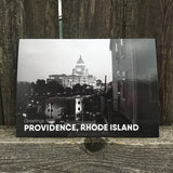 postcard of a black and white photograph of the RI state house at night behind some buildings and trees. white text reads "Providence, Rhode Island"