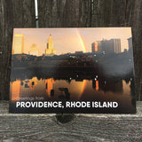 postcard phtoograph of the Providence skyline with a rainbow and white text on the bottom reading "Providence, Rhode Island"