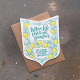 Die cut badge-shaped greeting card that reads "when life give you lemons, try to figure out something to do with those lemons" in teal text surrounded by illuatrated lemons and leaves