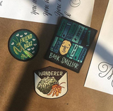 Moody sunlight illuminating three patches, a praying mantis that says friend to bugs, blue book smeller, and a hermit crab that says wanderer.