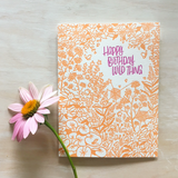 Greeting card and kraft paper envelope. Reads, "happy birthday wild thing" in whimsical, purple, handwritten font. Surrounded by illustration of a dense, wild garden of flowers, leaves and a few spiders.