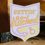 A greeting card with an envelope die-cut in the shape of badge with a Vegas style sign with text inside saying "gettin hitched" pointing at a ring. wedding, greeting card, cards, stationery, engagement