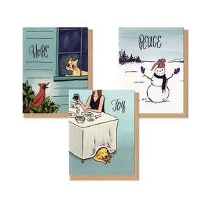 A set of 9 greeting cards, 3 of each style. From left to right: A greeting card featuring an orange cat in a window looking at a red cardinal on a bush with text that says Hope. A greeting card featuring a squirrel on top of a snowman who has stolen the carrot nose with Peace written above it. A greeting card with an illustration of a dinner table with a yellow dog under it who is eating a chicken leg with the word Joy above.