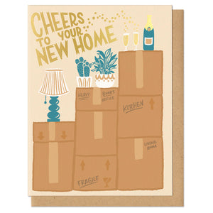 Greeting card and kraft paper envelope. Card reads, "cheers to your new home." Illustration of moving boxes stacked on each other with a lamp and two plants. On the tallest box is a champagne bottle and two champagne flutes.