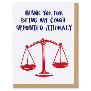 white greeting card that reads "thank you for being my court appointed attorney" in navy above a red illustration of old school scales