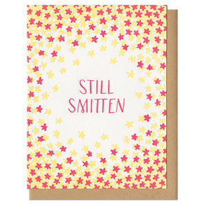 greeting card with a red and yellow star patter surrounded hand-letterinf that reads "still smitten"