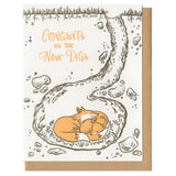 Greeting card and kraft paper envelope. Text reads "Congrats on the new digs." Illustration of cross section of the earth, with a fox den. Two foxes snuggling in their underground den.