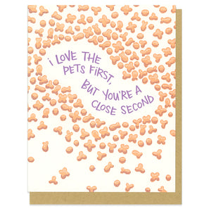 A greeting card and envelope featuring cat and dog kibble in orange with purple text in the middle that says "I love the pets first, but you're a close second."