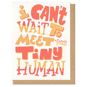 Greeting card with kraft envelope. Card reads "I can't wait to meet your tiny human" in hand-drawn festive block letters in various sizes and patterns in yellow and orange.
