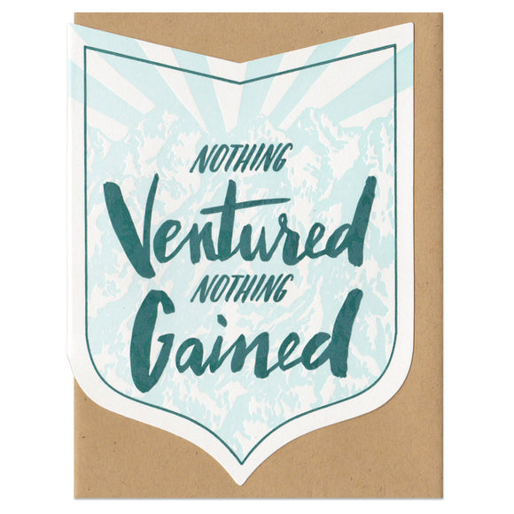 badge-shaped greeting card with a light blue illustration of a mountain range behind green hand-lettering that reads 