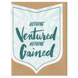 badge-shaped greeting card with a light blue illustration of a mountain range behind green hand-lettering that reads "nothing ventured nothing gained"