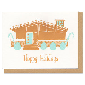 A greeting card and envelope featuring an illustration of a gingerbread house wirh text under that says "happy holidays"