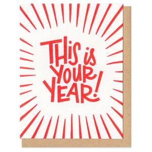 white greeting card with red lines and hand-lettering that reads "this is your year!"