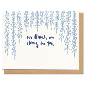 white horizontal greeting card with light blue illustrated dangling willow branches with navy hand-lettering that reads "our hearts are heavy for you"