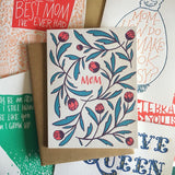 white greeting card with red  hand-lettering that reads "mom" surrounded by red and green illustrated tulips pictured on an assortment of Frog & Toad press greeting cards