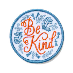 A circular iron on patch with blue floral and a coral script that reads "be kind".