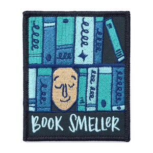 A rectangle patch with a face surrounded by various shades of blue books with text under it that says, "book smeller" on a white background.