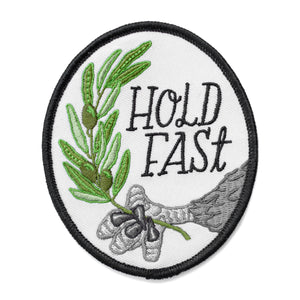 An oval iron on embroidered patch featuring an eagle's claw holding an olive branch with script text next to it that says, "Hold fast."