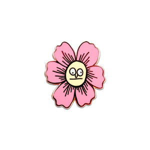 An enamel pin with a butterfly back in the shape of a pink flower with a very silly indifferent face in the center