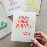 white greeting card which reads "you're going to be great parents! can you adopt me next?" in red with a circle of yellow stars shown held above other cards