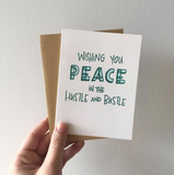 hand holding a white greeting card with teal handlettering which reads "wishing you peace in the hustle and bustle"