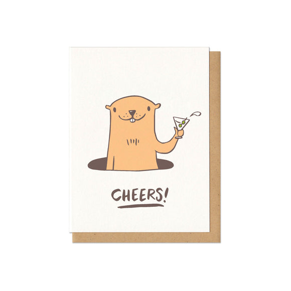Greeting card with kraft paper envelope. Illustration of groundhog emerging from hole, smiling and holding a martini glass. (extra dry, two olives.) Text below reads, 