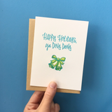 A greeting card and envelope featuring script that says "Happy holidays, ya ding dong" with a green bell below it.