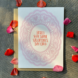 Greeting card and kraft paper envelope. Illustration of pink, lacey doily. At the center the handwritten text reads, "Here's your damn Valentine's Day card."