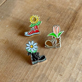 An enamel pin with a rubber backer in the shape of a Doc Marten black boot with a white daisy coming out of it. floral, flowers, daisies, boots, 90s, pins, button, pin, enamel pin, accessories, flair
