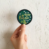 An iron on embroidered circle patch with a black outline and a forest green background with a praying mantis, flies, and text that reads "friend to bugs" against a white wood background
