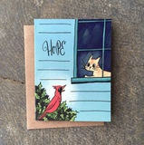 A greeting card featuring an orange cat in a window looking at a red cardinal on a bush with text that says Hope. 