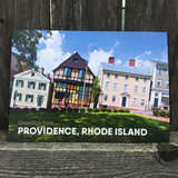 postcard photograph of very colorful historic buildings in daylight above white text that reads "greetings from providence, rhode island"
