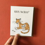 white greeting card thaht read "where you been?" above an illustration of a tiger with a man in his belly photographed hand-held in front of a red background