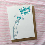Greeting card and craft envelope that reads "welcome peanut!" in teal, hand-written type in upper right corner. Illustration of elephant trunk shaking rattle.