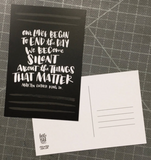 A black postcard with handlettered text reading, "Our lives begin to end the day we become silent about the things that matter. - Martin Luther King, Jr"