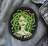 A patch of a green medusa with snakes for hair and "don't mess" below her against a denim jacket. patch, patches, mythology, snakes, greek, accessories, flair