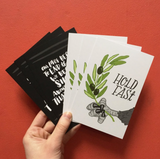 A set of 6 postcards, 3 postcards that have an eagle holding an olive branch with text that says "Hold fast", and 3 black postcards with handlettered text reading, "Our lives begin to end the day we become silent about the things that matter. - Martin Luther King, Jr"